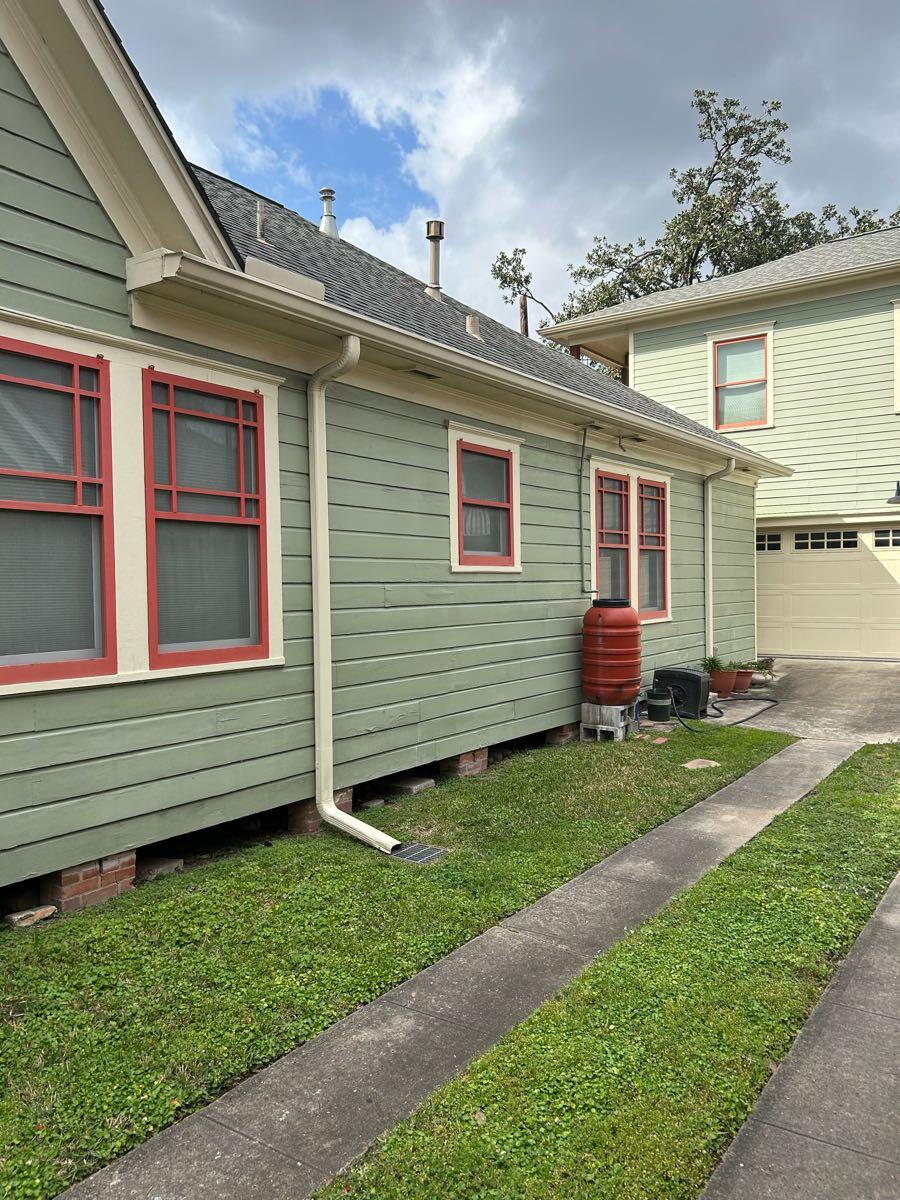 Side and rear elevations of a green Houston home with lap siding, white trim, and a detached garage